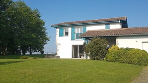 Une maison à deux étages, avec une façade blanche et des volets bleus, un toit en tuiles et un petit porche à l’avant.