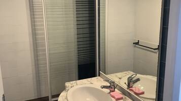 Une salle de bain avec un lavabo blanc, un miroir et une cabine de douche en verre.