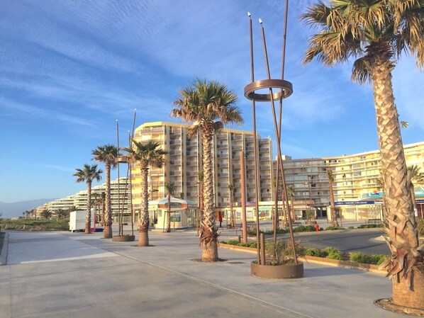 A hotel with a modern design, featuring a curved facade, multiple balconies, and palm trees in the foreground.