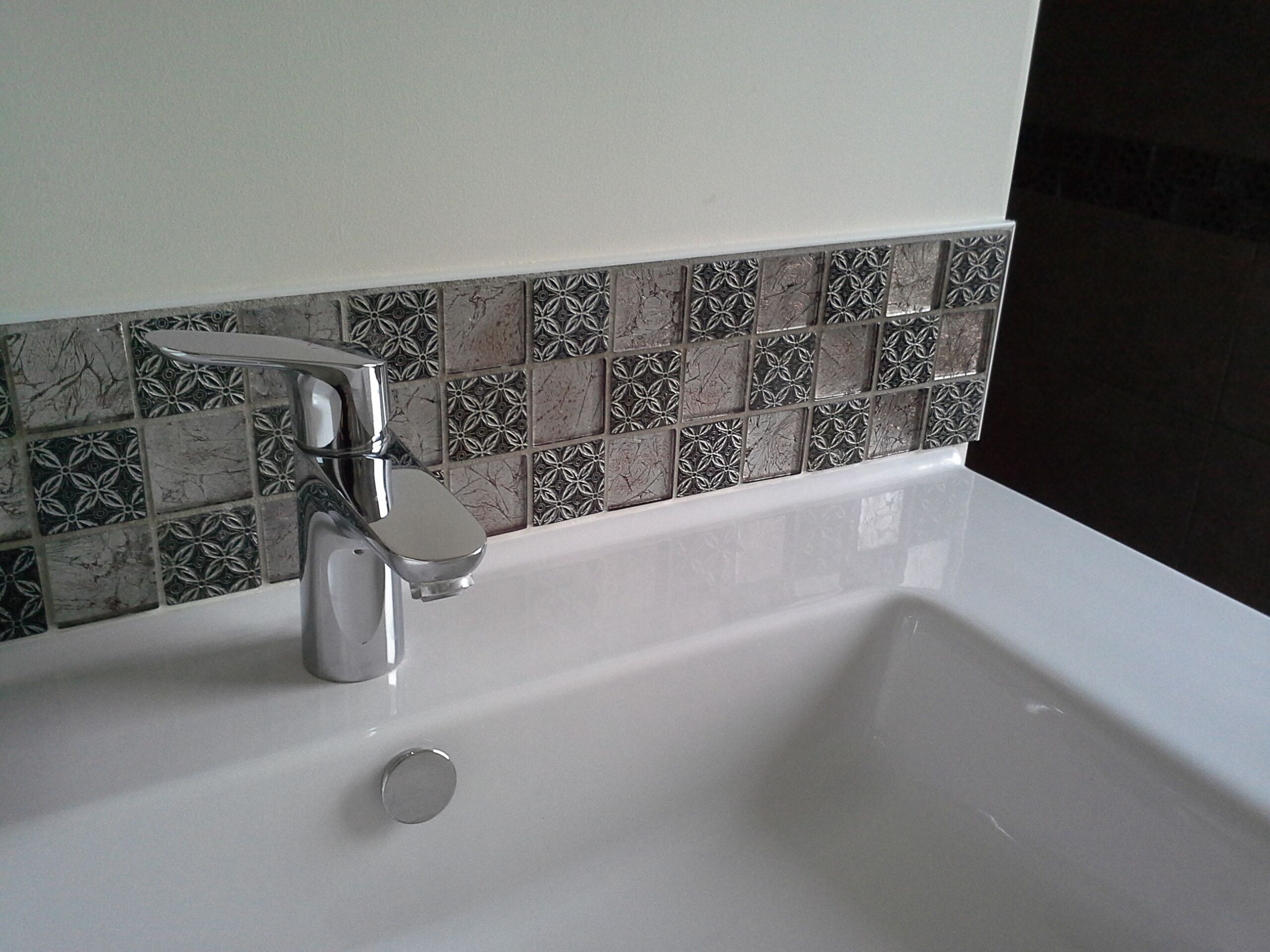 A bathroom sink with a modern faucet and a decorative tile backsplash.