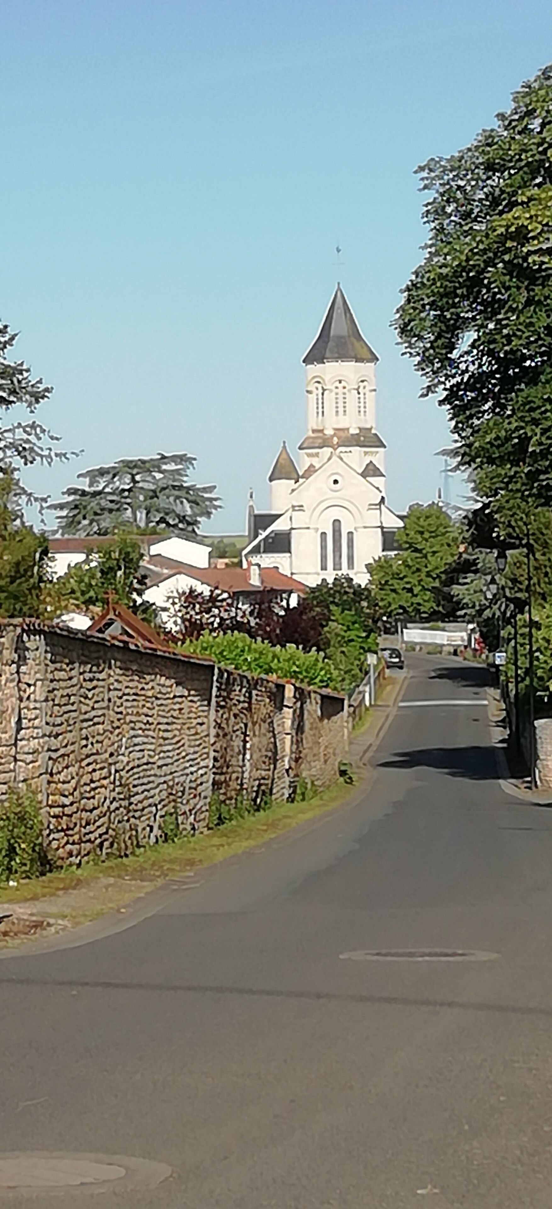 Uma rua que leva a uma igreja com uma torre alta e um muro de pedra de um lado.