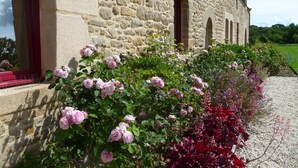 Een stenen gebouw met boogvensters en een tuin vol roze en rode bloemen.