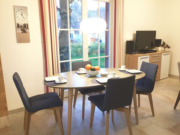 Un comedor con una mesa redonda, seis sillas, un frutero y un televisor al fondo.