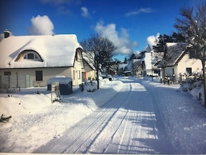 A snow-covered street with houses, a clear sky, and a visible road.