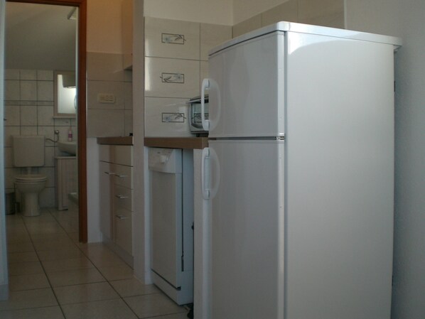 A kitchen with a white refrigerator, a microwave, and a built-in oven. There is a sink and a toilet visible in the background. - few minutes to the beach (Postira)