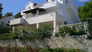 A two-story white building with a stone wall in front, balconies, and a clear blue sky. - few minutes to the beach (Postira)