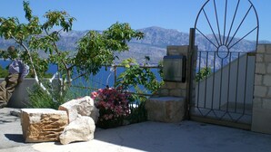 A stone gate with a metal design, a view of mountains, and a body of water in the background. - few minutes to the beach (Postira)