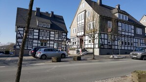 Un bâtiment traditionnel à colombages, orné d’une enseigne « Volksbank », avec des voitures garées et un ciel dégagé.