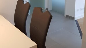 Une pièce moderne avec une table blanche et deux chaises, une porte vitrée et un sol carrelé.