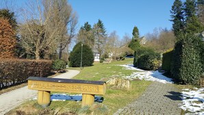 Un parc avec un banc en bois, des allées pavées et des plaques de neige.