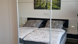 Une chambre à coucher moderne avec un lit, une table de chevet, un miroir et une décoration murale sur le thème de la forêt.
