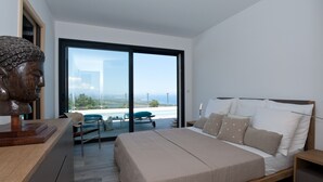 A modern bedroom with a large bed, a wooden headboard, a wooden desk, and a view of the cityscape through a large window.