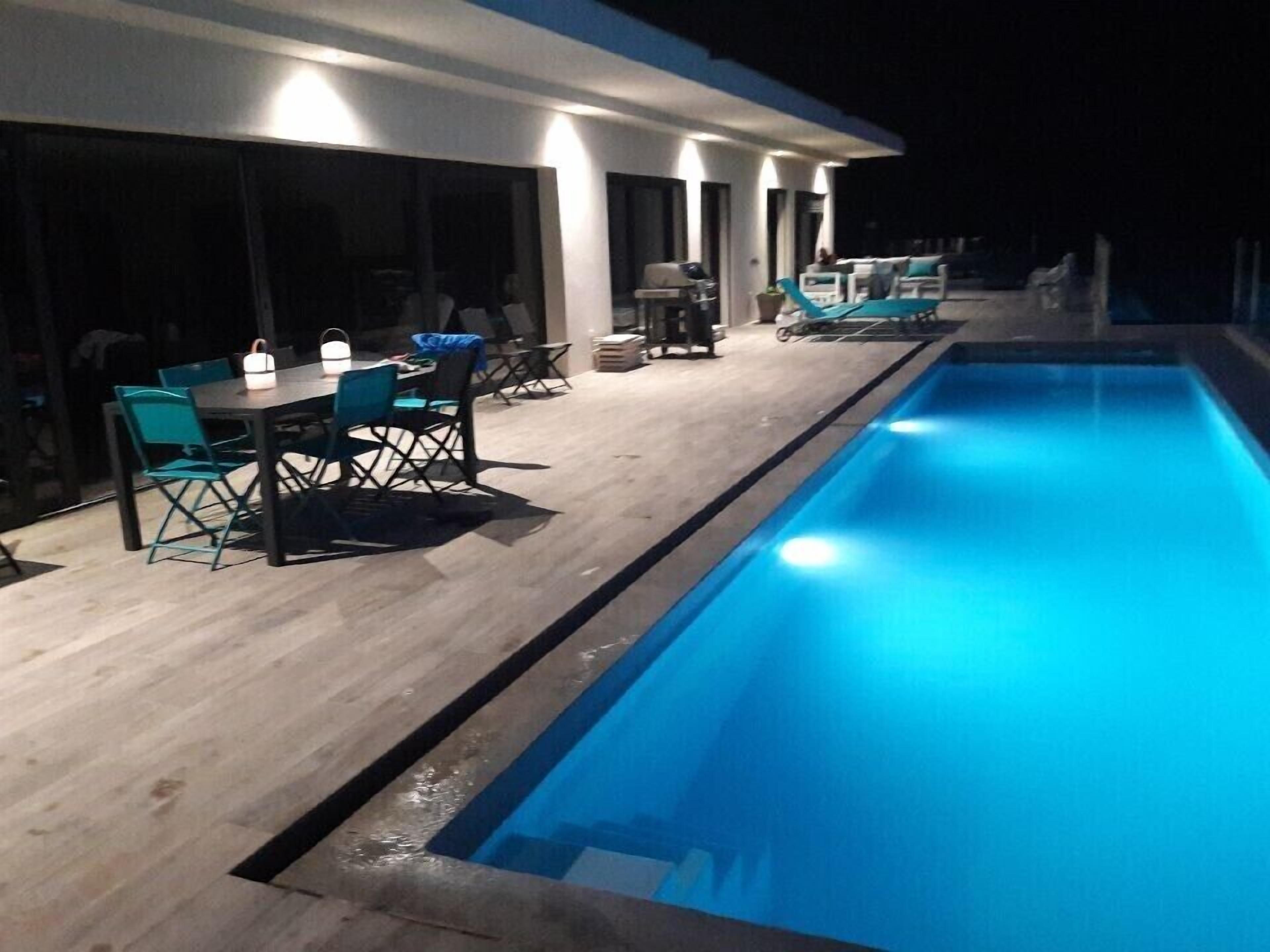 Un espace aménagé au bord de la piscine, comprenant une table et des chaises pour les repas, un barbecue et des chaises longues.
