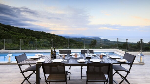 An outdoor dining area with a view of a pool and hills.