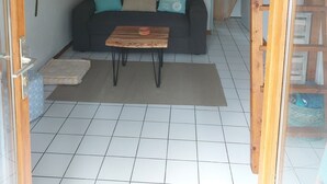 Un salon chaleureux avec un plafond en bois, un canapé noir agrémenté de coussins turquoise, une table basse en bois et un petit tapis.