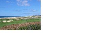 Un parcours de golf offrant une vue dégagée sur l’océan et une plage de sable en arrière-plan.