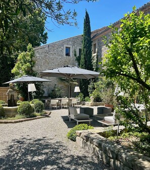 An outdoor patio with stone tables and chairs, umbrellas, and a fountain. - LARGE CHARMING HOUSE ON THE DOMAINE DE SAINT DOMINGUE (Narbonne)