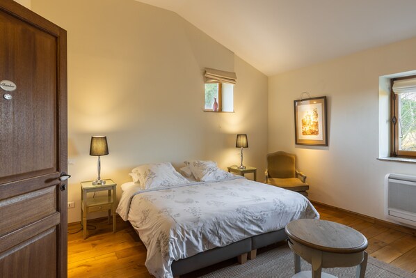 A bedroom with a bed, bedside lamps, a chair, a small table, a window with a view, and a radiator. - LARGE CHARMING HOUSE ON THE DOMAINE DE SAINT DOMINGUE (Narbonne)