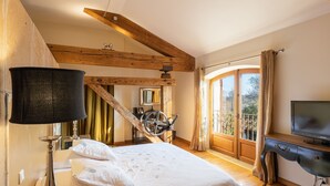 Een slaapkamer met een bed, een televisie, een lamp en een groot raam met gordijnen.