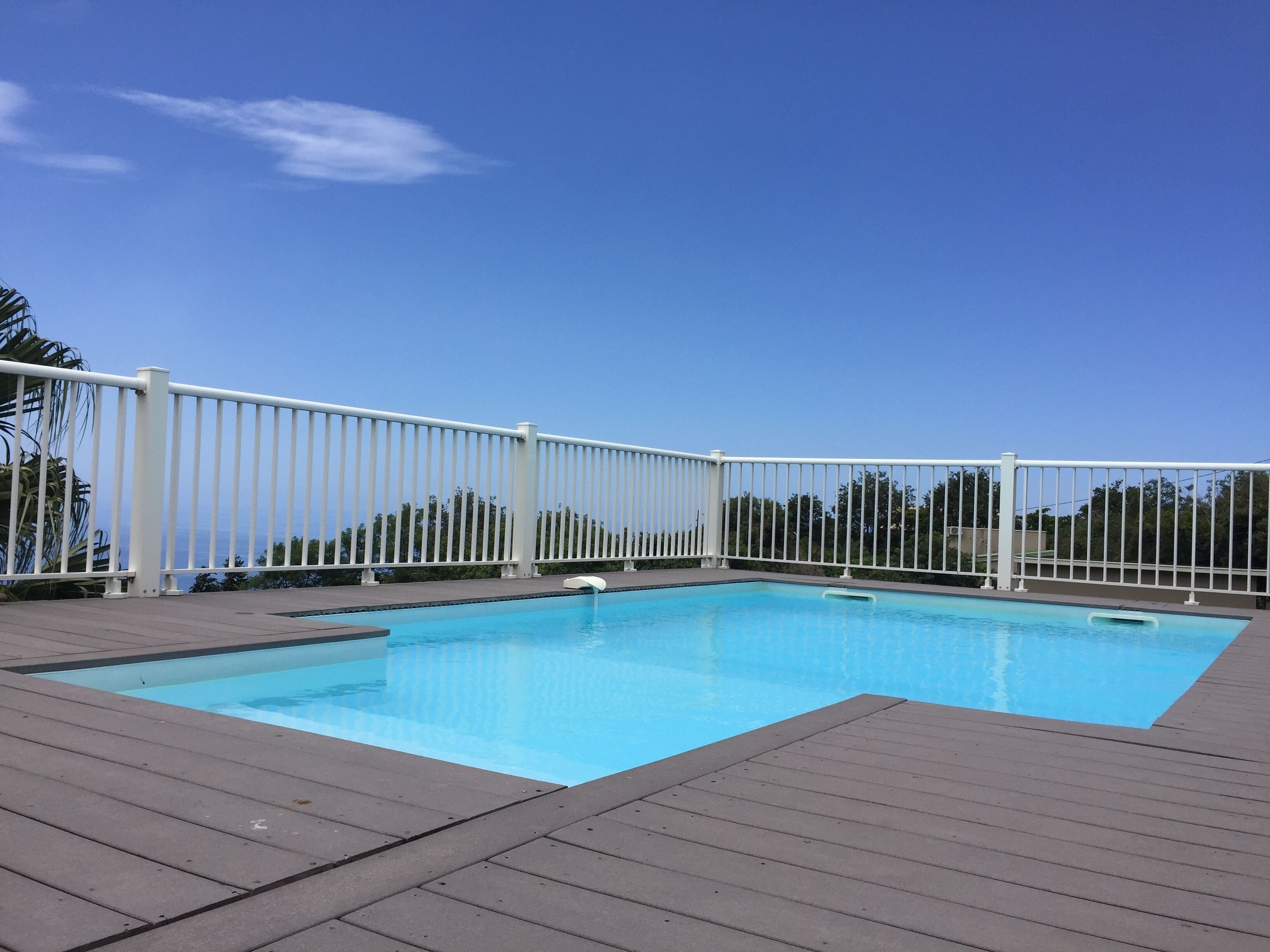 A rectangular swimming pool with a white fence surrounding it, set on a wooden deck.