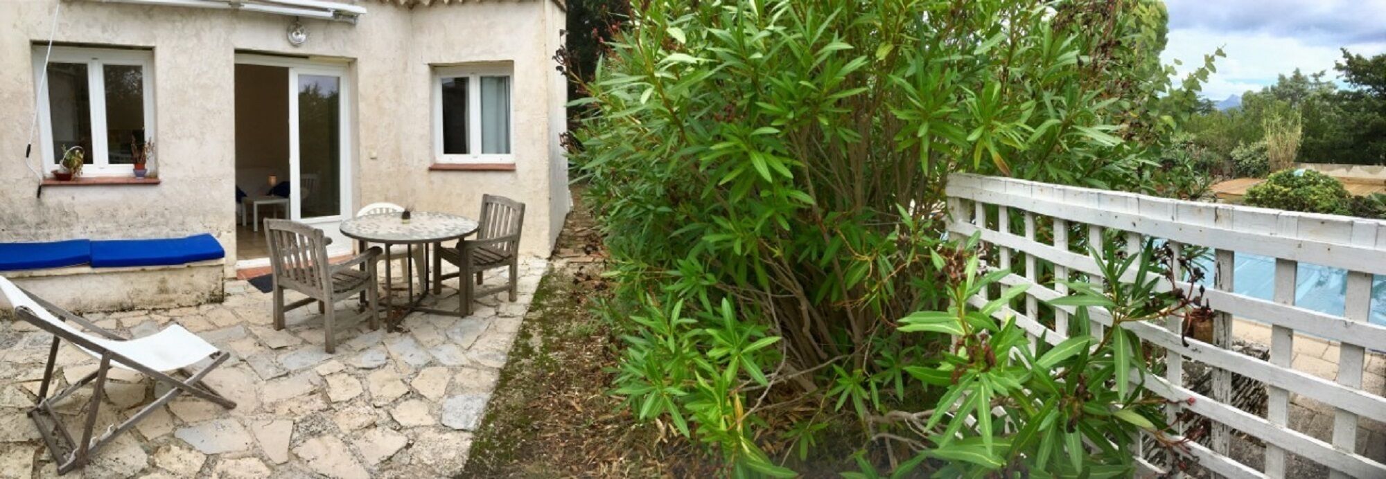 Un patio con una mesa y sillas, una cerca blanca y una planta verde exuberante.
