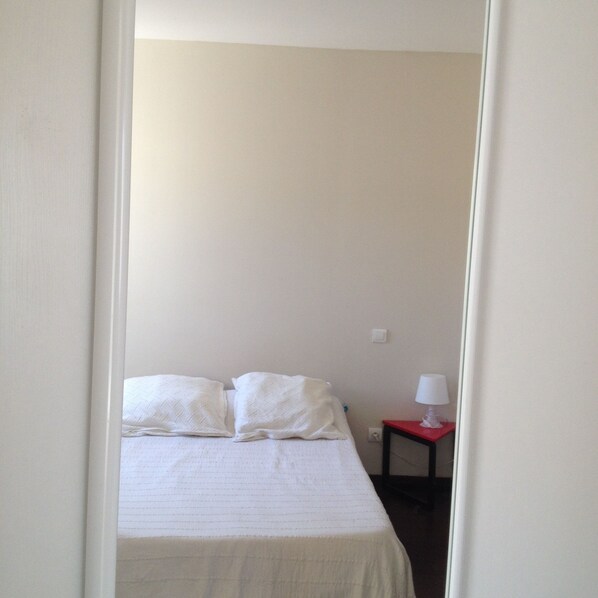 A simple, unadorned bedroom with a bed, pillows, and a nightstand with a lamp. - NEAR CASSIS. HOUSE T2 COZY ISOLATED AT THE BOTTOM OF GARDEN (Carnoux-en-Provence)