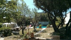 Un patio trasero con piscina, plantas en macetas y mobiliario exterior.