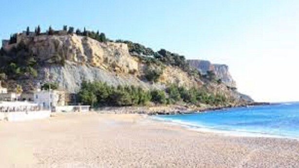 Una playa con un acantilado rocoso y un edificio a la izquierda.