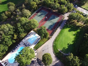Ein Luftbild eines Sportkomplexes mit Tennisplätzen, einem Schwimmbecken und umgebender Bepflanzung.
