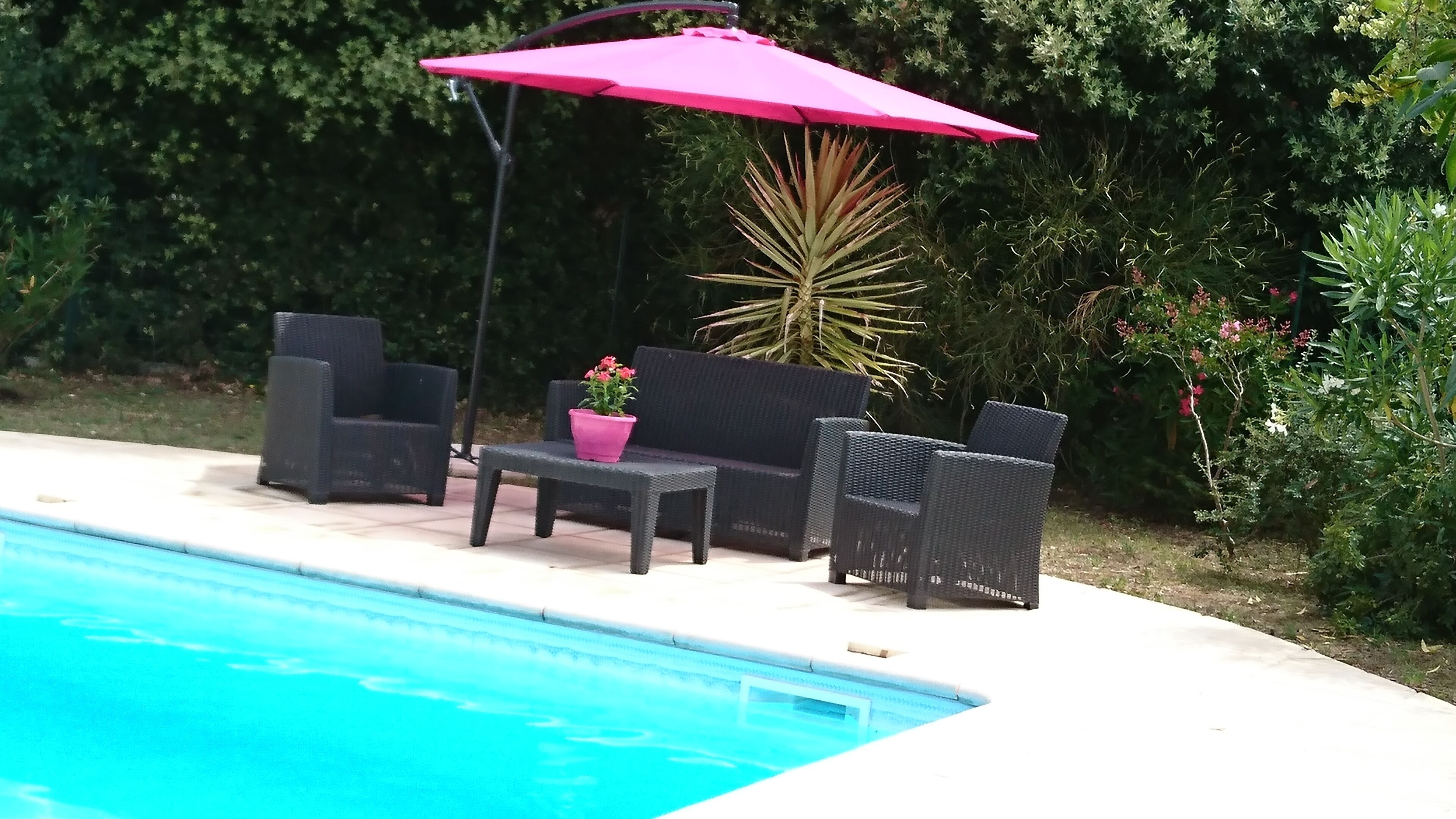 Zona de piscina amb seients, cadires, una taula, un parasol rosa i una planta en test.