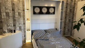 Een slaapkamer met een bed, een nachtkastje, een plank met klokken en een plant.