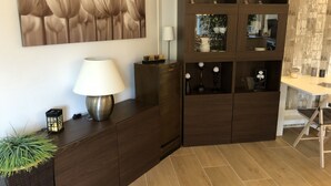 Een moderne woonkamer met een donker houten kast, een lamp, een aan de muur hangend schilderij en een inbouwkast met decoratieve objecten.