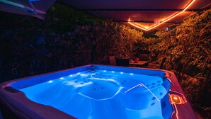 A hot tub with a blue light, surrounded by plants and under a covered area.