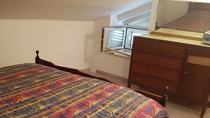 Un dormitorio con cama, cómoda, ventana con persianas y una lámpara en el techo.