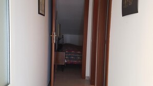 Un pasillo estrecho con una cama al fondo, una puerta a la izquierda y una pared decorada con un cuadro.