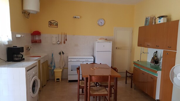 Cocina compacta con lavadora, estufa y refrigerador. Cuenta con una mesa de comedor, sillas y un ventilador de techo.