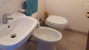 Un baño con lavamanos, bidé, inodoro y un perchero para toallas.