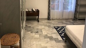 A bedroom with a bed, a wardrobe, a chest of drawers, a wicker basket, a rug, and a window with curtains. - 3 room apartment on the ground floor of a villa with sea view (Mandelieu-La-Napoule)