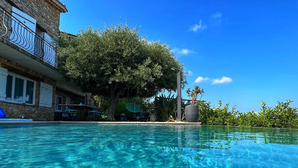 A clear swimming pool with a stone building and a tree in the background. - 3 room apartment on the ground floor of a villa with sea view (Mandelieu-La-Napoule)