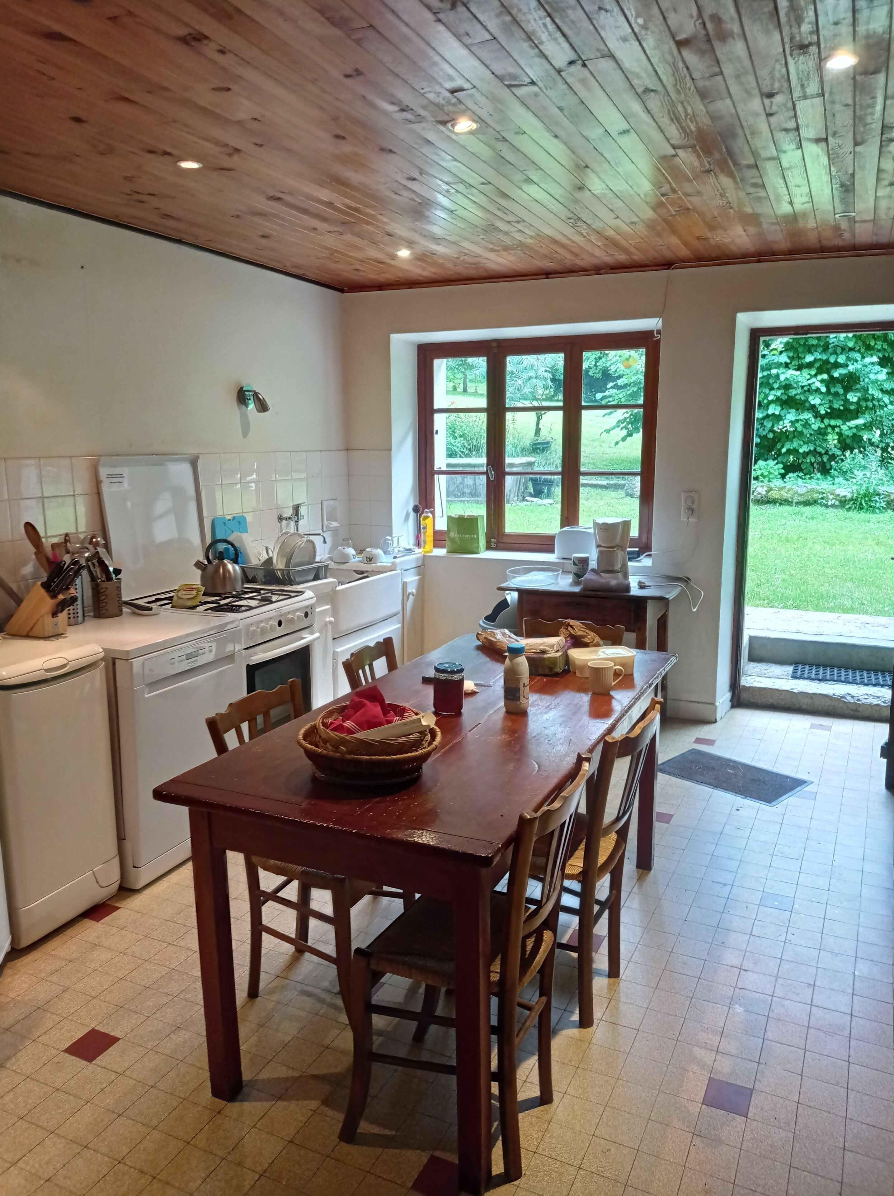 Een keuken met een houten plafond, een eettafel met stoelen en uitzicht op een tuin door een raam.