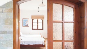 A bedroom with a wooden door, a bed with a white bedspread, a map on the wall, and a window with a wooden frame. - Charming cottage with a unique view (Episkopi Rethymnon)