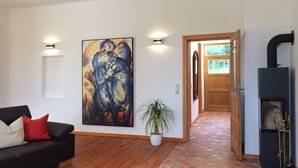 Un salon avec un canapé noir, un grand tableau abstrait, une plante en pot et un poêle à bois.