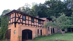 Un bâtiment traditionnel à colombages, doté d’une façade en briques et d’une structure en bois apparent, entouré de verdure et d’arbres.