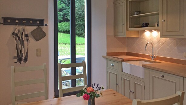 Une cuisine avec une table à manger, des chaises, un vase de fleurs et une vue sur la verdure à l’extérieur.