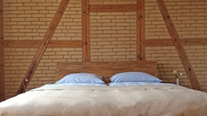 Un lit avec une tête de lit en bois et deux oreillers, dans une pièce aux murs en briques apparentes et aux poutres en bois.