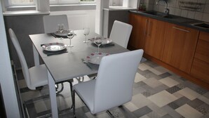 A dining area with a table set for four, including plates, glasses, and cutlery. There are white chairs around the table, and a kitchen area with wooden cabinets and a sink is visible in the background. - Colmar, close to the center, charming 3-room apartment in a quiet area (Colmar)