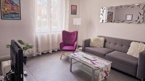 A living room with a purple armchair, a grey sofa, a glass coffee table, a flat-screen TV, and a painting of a bridge. - Colmar, close to the center, charming 3-room apartment in a quiet area (Colmar)