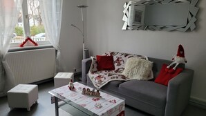 A living room with a grey sofa, a glass coffee table, a white ottoman, and a red and white patterned blanket. - Colmar, close to the center, charming 3-room apartment in a quiet area (Colmar)