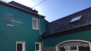 A teal building with a tiled roof, a door labeled 'Bodenbelage Tapeten Farben,' and a window with a sign 'www.westerburger-farbenwelt.de'. - Vacation apartment Westerburg for 1-3 persons in Westerburg city center (Westerburg)