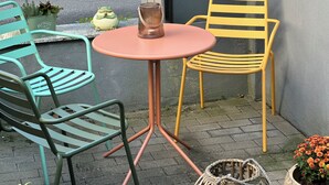 A small outdoor seating area with a round table and two chairs, one green and one yellow, near a wall. - Vacation apartment Westerburg for 1-3 persons in Westerburg city center (Westerburg)